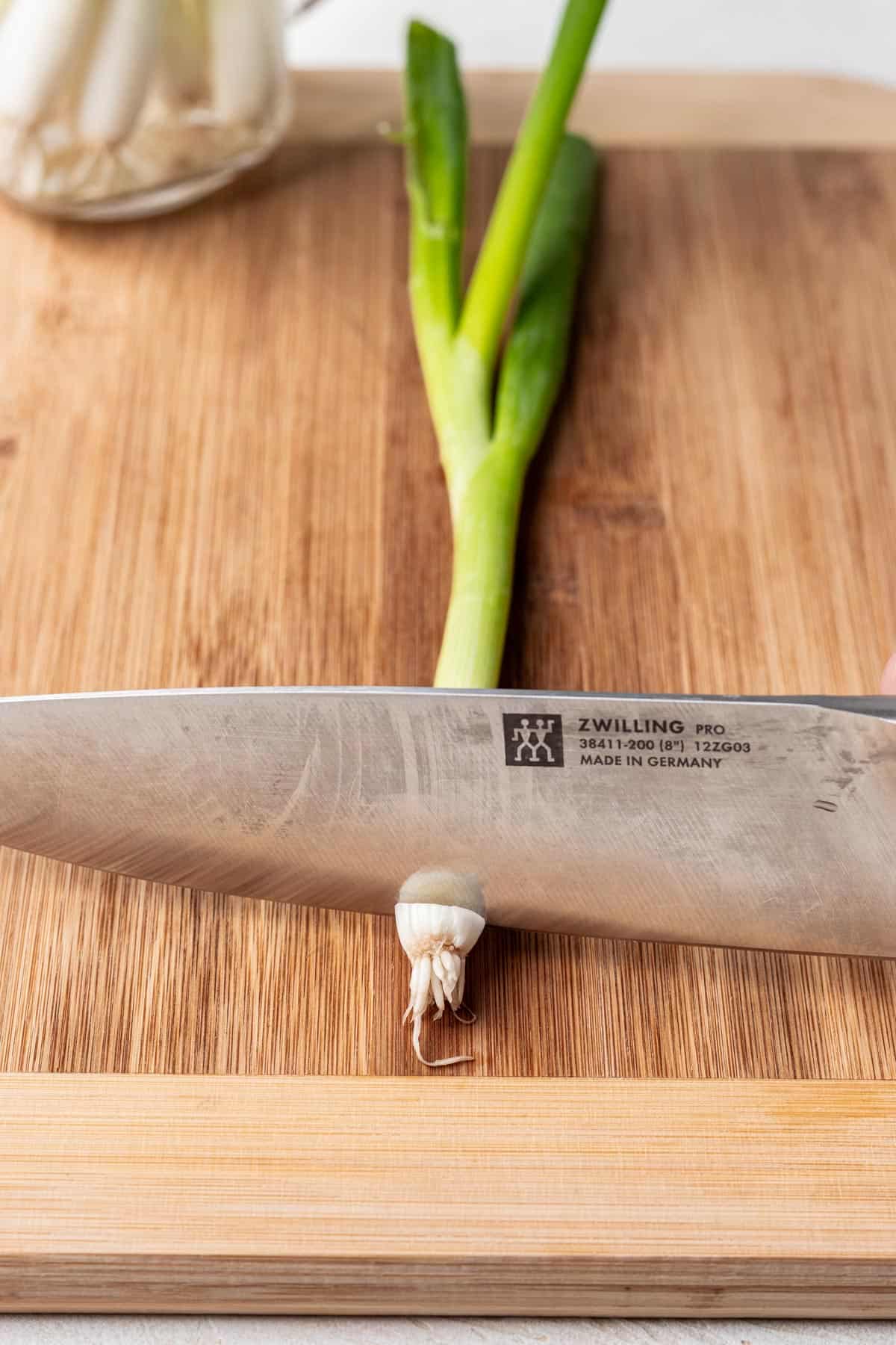 A knife slicing the end off a green onion.