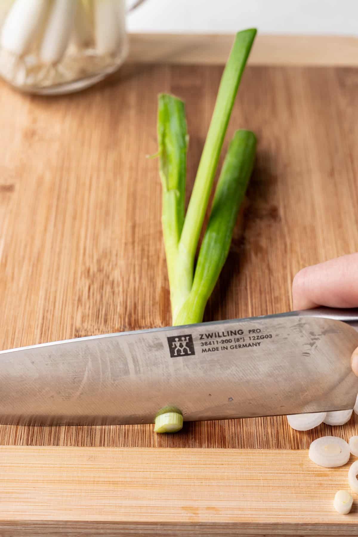 A knife slicing the white part of a green onion.