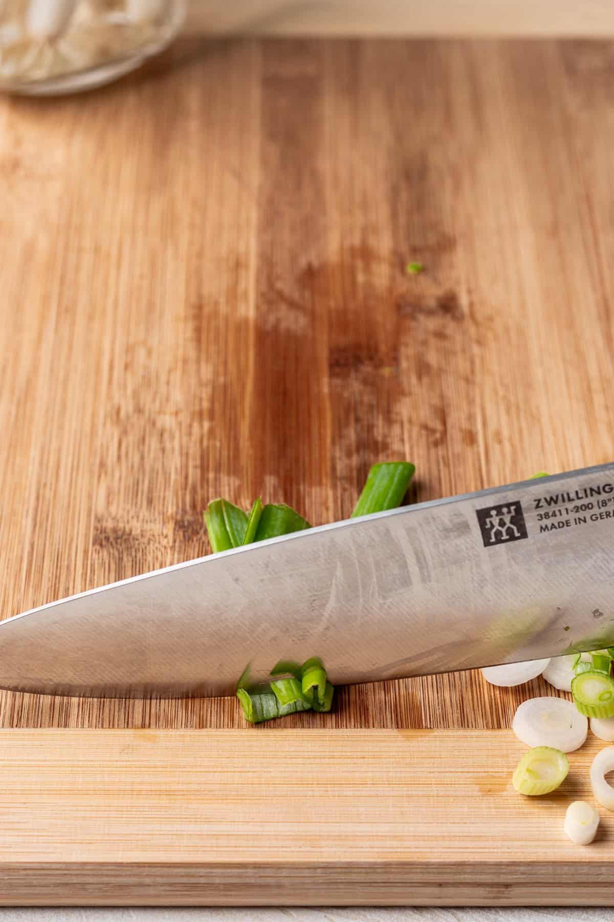 A knife slicing the green part of a green onion.