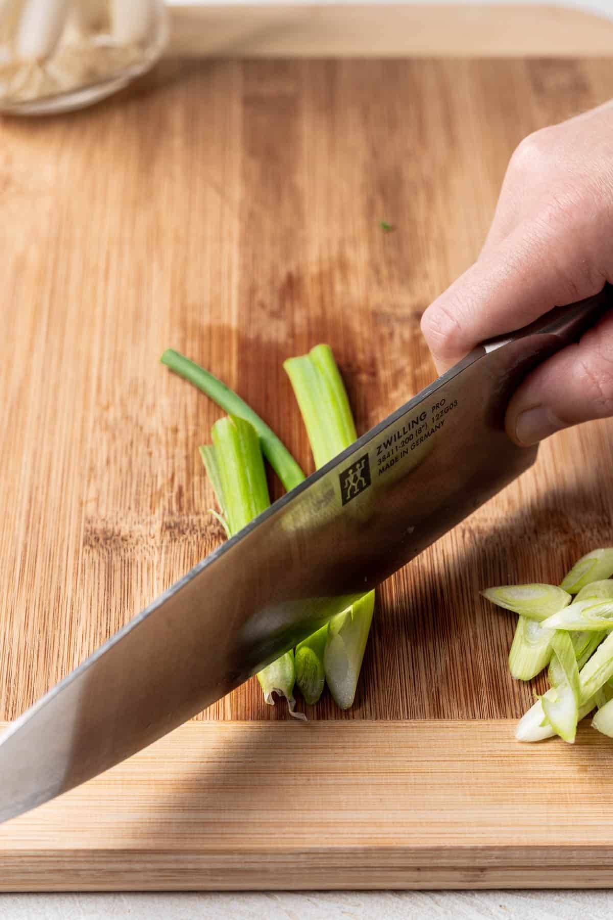 A knife slicing green onion on a bias.