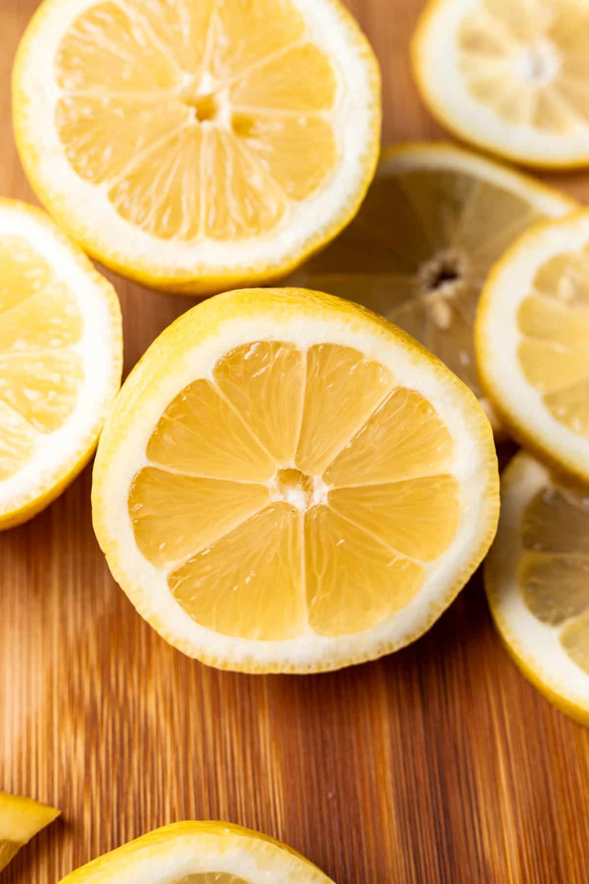 Half a lemon with lemon slices around it on a cutting board.