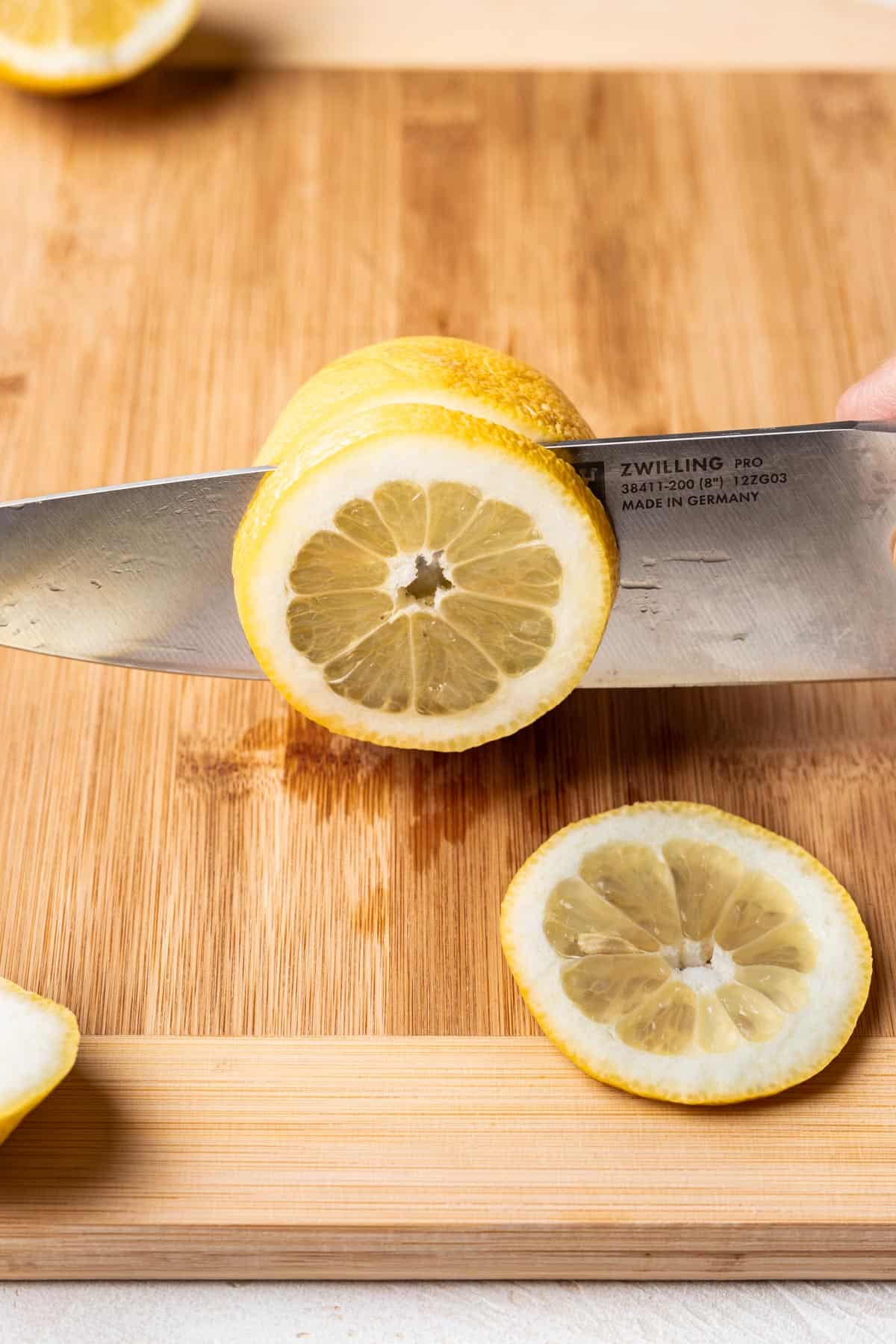 A sharp chef's knife cutting lemon slices.