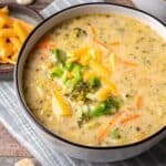 Instant pot broccoli cheddar soup in a white bowl topped with cheddar cheese and green onions.