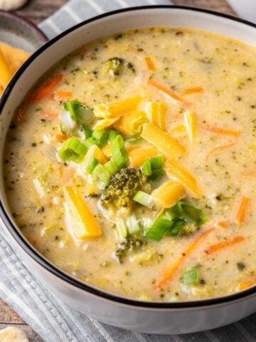 Instant pot broccoli cheddar soup in a white bowl topped with cheddar cheese and green onions.