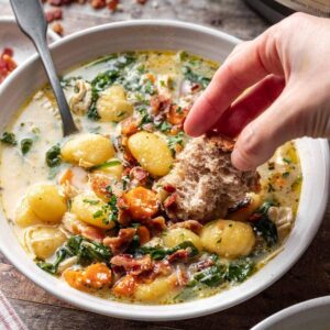 Instant pot chicken gnocchi soup in a bowl with a hand dipping bread into it.