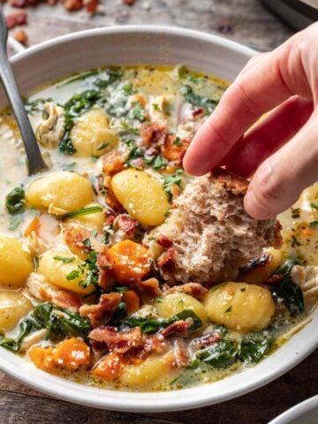 Instant pot chicken gnocchi soup in a bowl with a hand dipping bread into it.