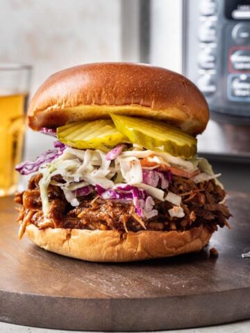 Shredded instant pot pork butt on a bun with slaw and pickles.