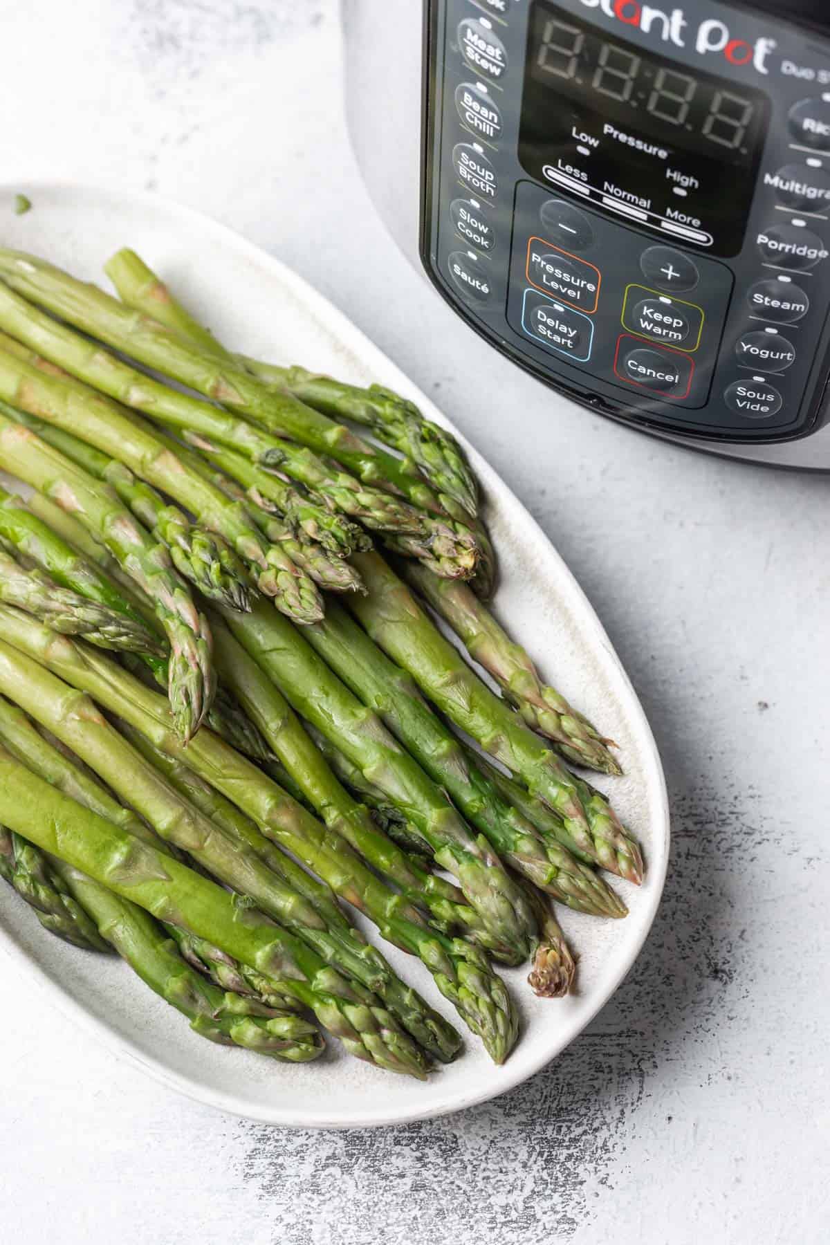 Cooked asparagus on a serving platter in front of an instant pot.