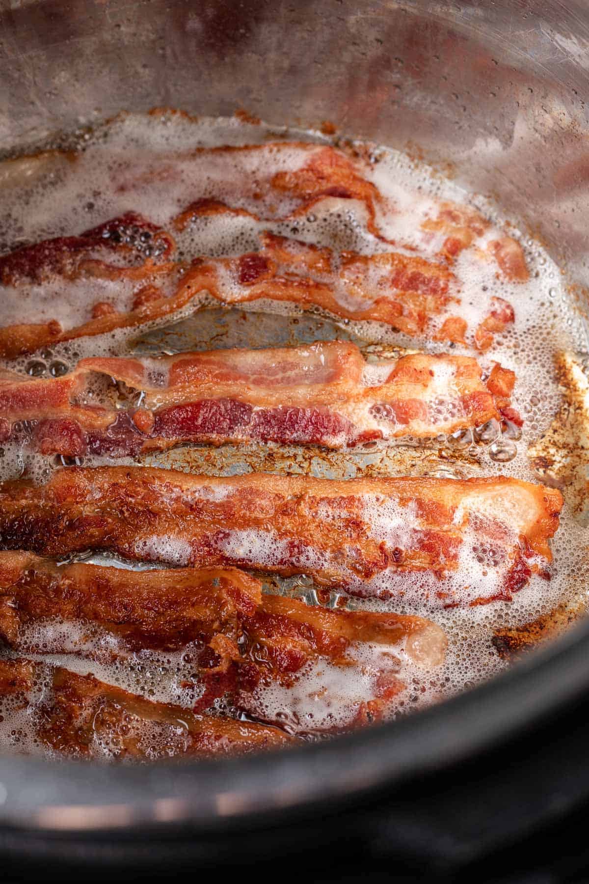 Bacon cooking in an instant pot with bubbly bacon grease.