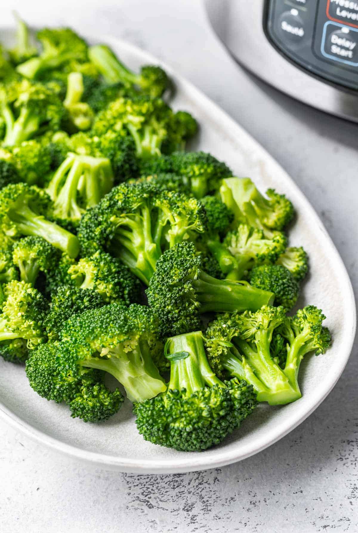 Instant pot broccoli on a serving platter with an instant pot behind it.