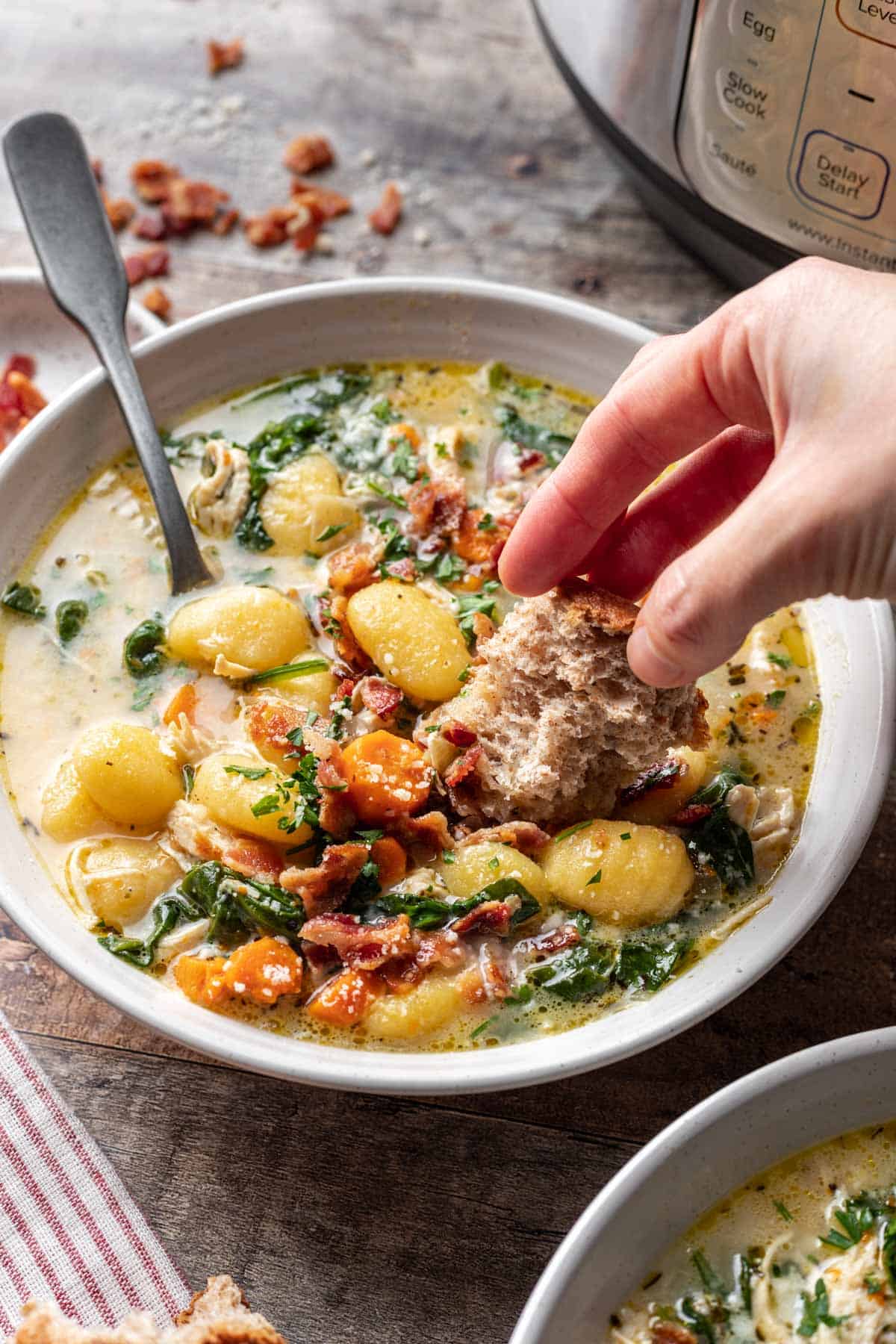 Instant pot chicken gnocchi soup in a bowl with a hand dipping bread into it.