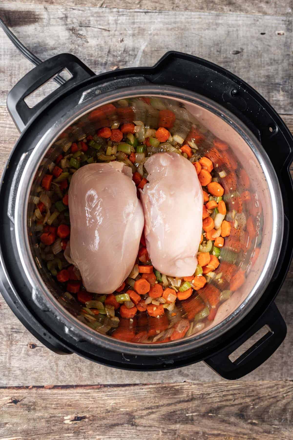 Raw chicken on top of carrots, onion, and celery in an instant pot.