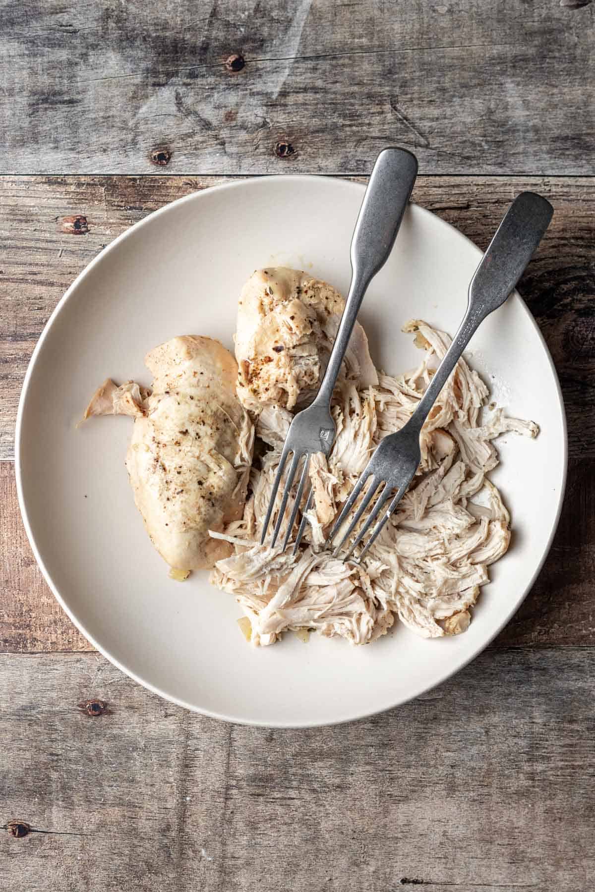 Chicken shredded by 2 forks in a bowl.