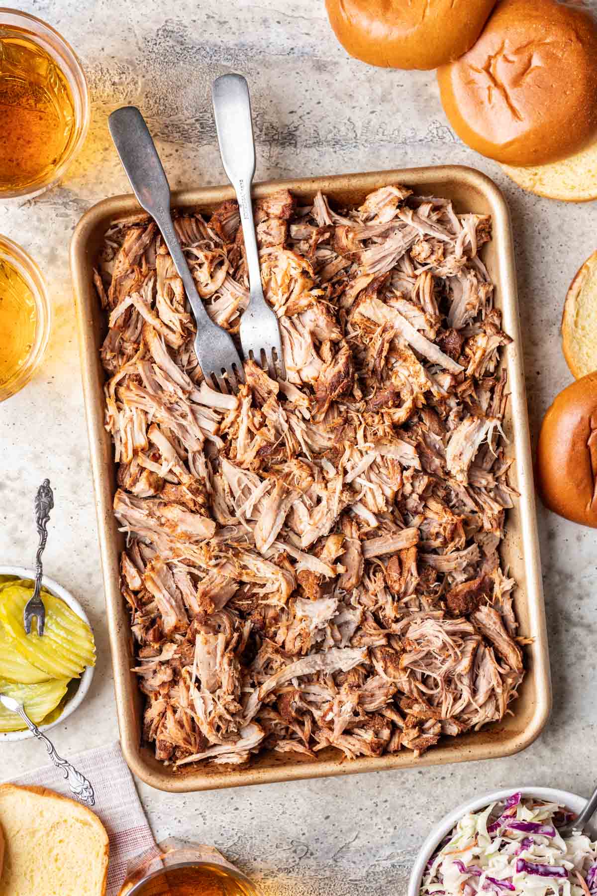 Shredded pork butt on a tray with sandwich fixings around it.