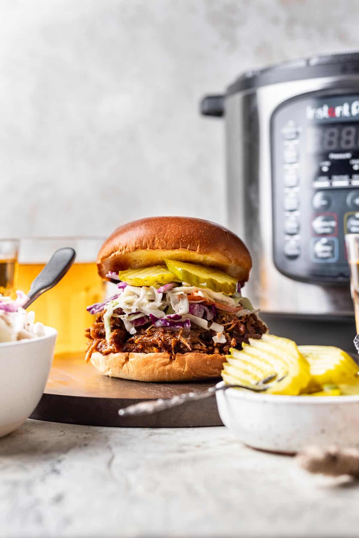 Shredded instant pot pork butt in sauce on a bun with pickles and slaw.