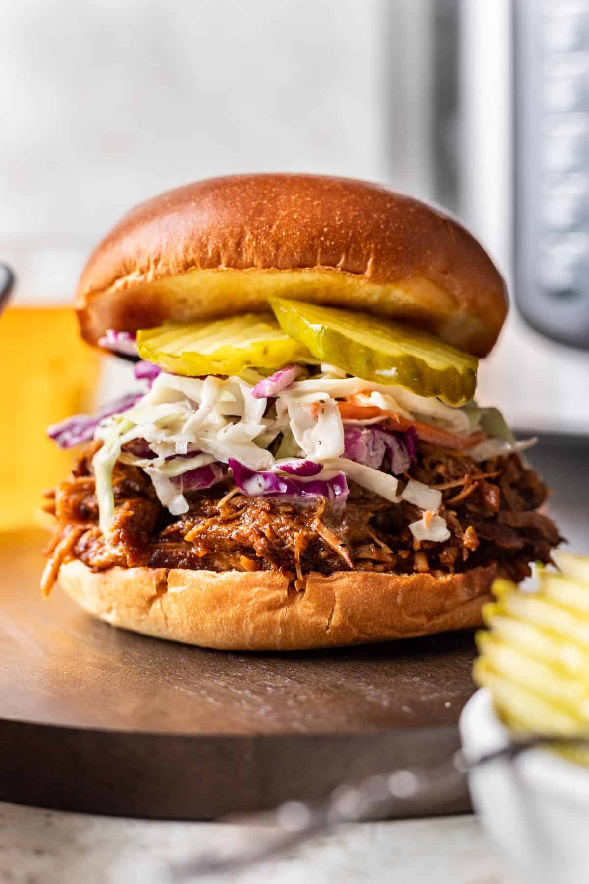 Shredded instant pot pork butt on a bun with slaw and pickles.