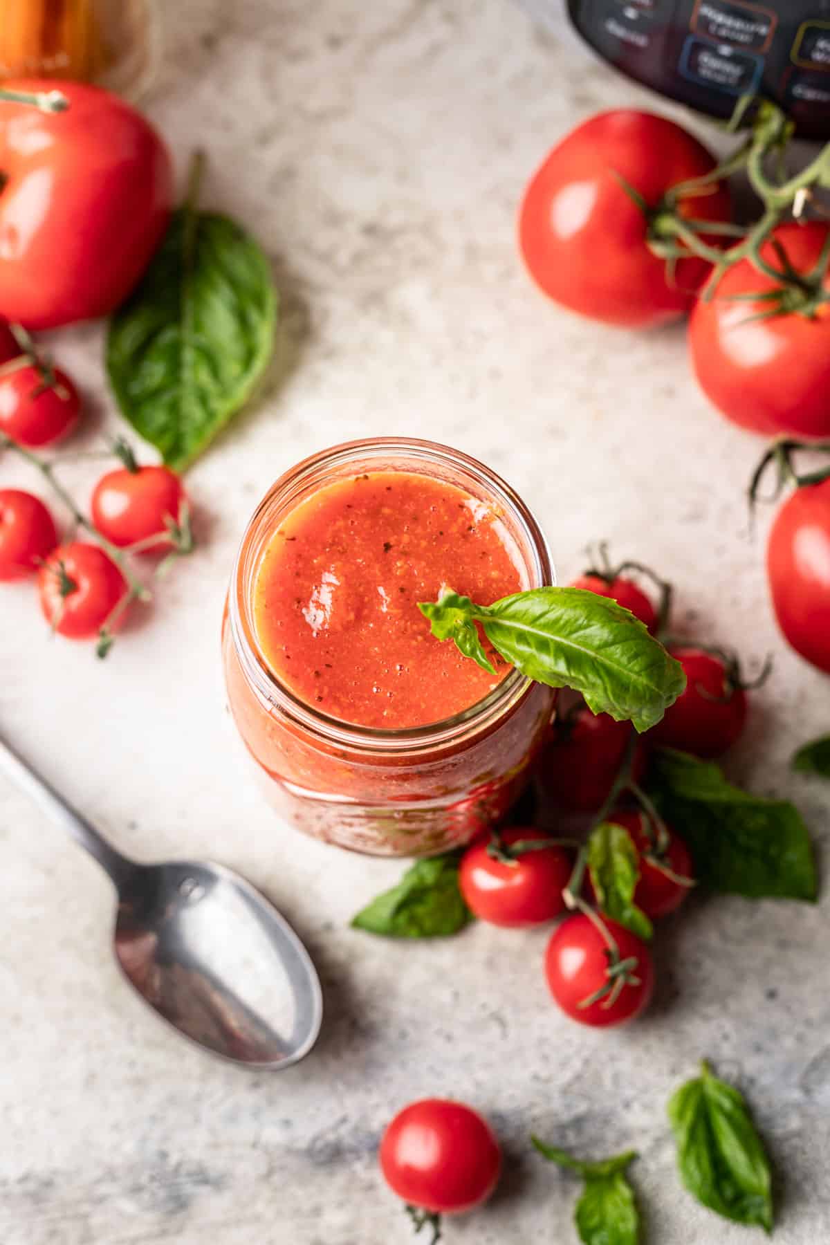 Instant pot tomato sauce in a glass jar with fresh basil and tomatoes.