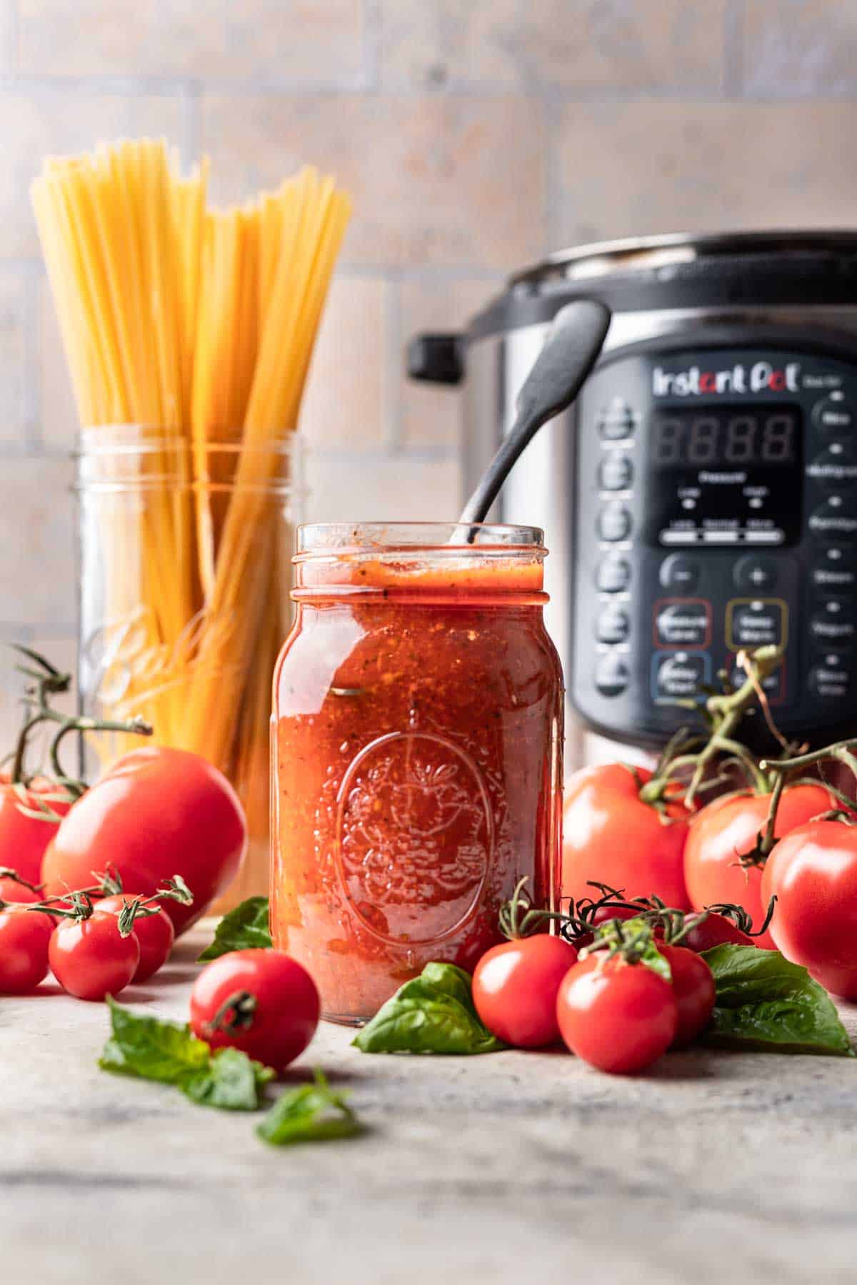 Instant pot tomato sauce in a jar with spaghetti noodles and tomatoes around it.