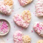 Pink and white chocolate covered heart shaped rice krispie treats on parchment paper.