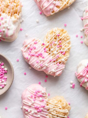 Pink and white chocolate covered heart shaped rice krispie treats on parchment paper.