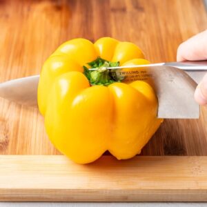 A yellow bell pepper getting cut in half with a chef's knife.