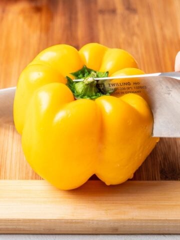 A yellow bell pepper getting cut in half with a chef's knife.