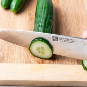 A cucumber being sliced on a cutting board.