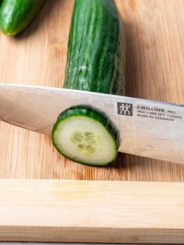 A cucumber being sliced on a cutting board.