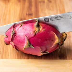A chef's knife cutting a dragon fruit in half.