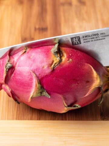 A chef's knife cutting a dragon fruit in half.