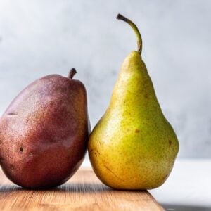 A red and green pear on a wood cutting board.