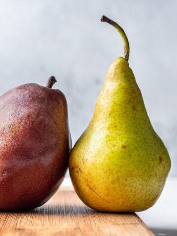 A red and green pear on a wood cutting board.