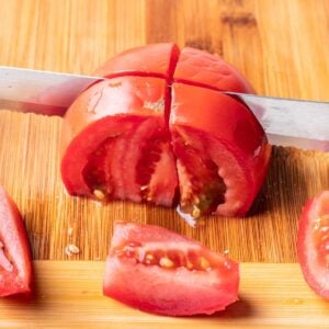 A chef's knife cutting a tomato into wedges.