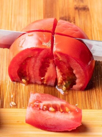 A chef's knife cutting a tomato into wedges.