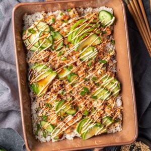 Salmon sushi bake in a baking dish topped with avocado and spicy mayo.