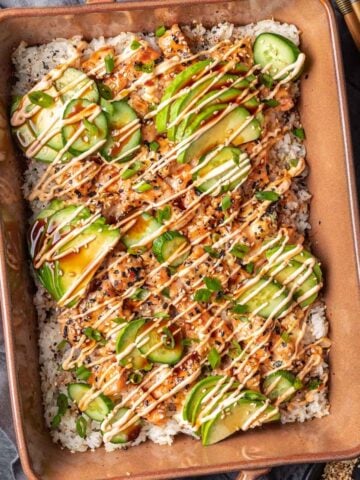 Salmon sushi bake in a baking dish topped with avocado and spicy mayo.