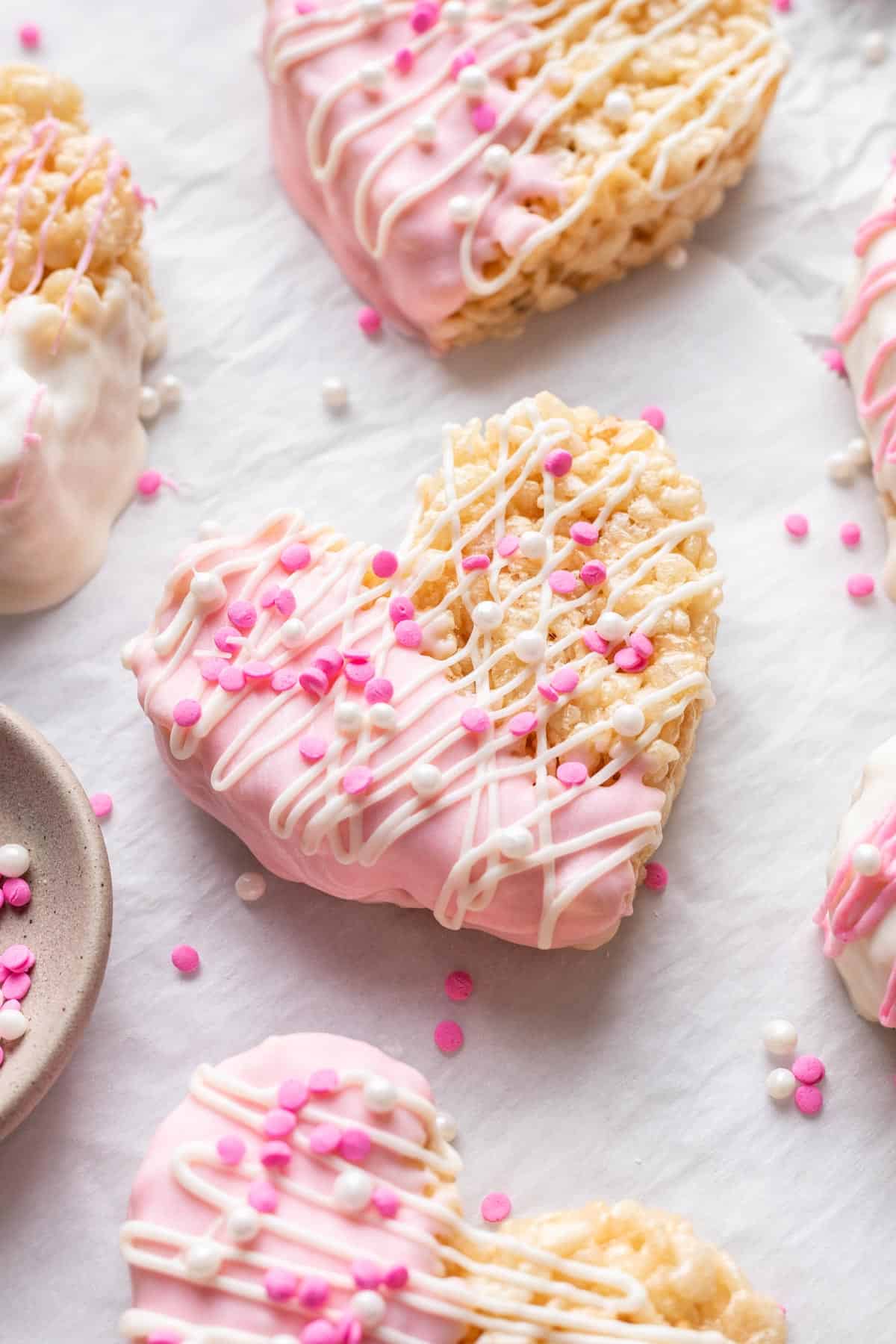 Heart shaped rice krispie treats on parchment paper with sprinkles.