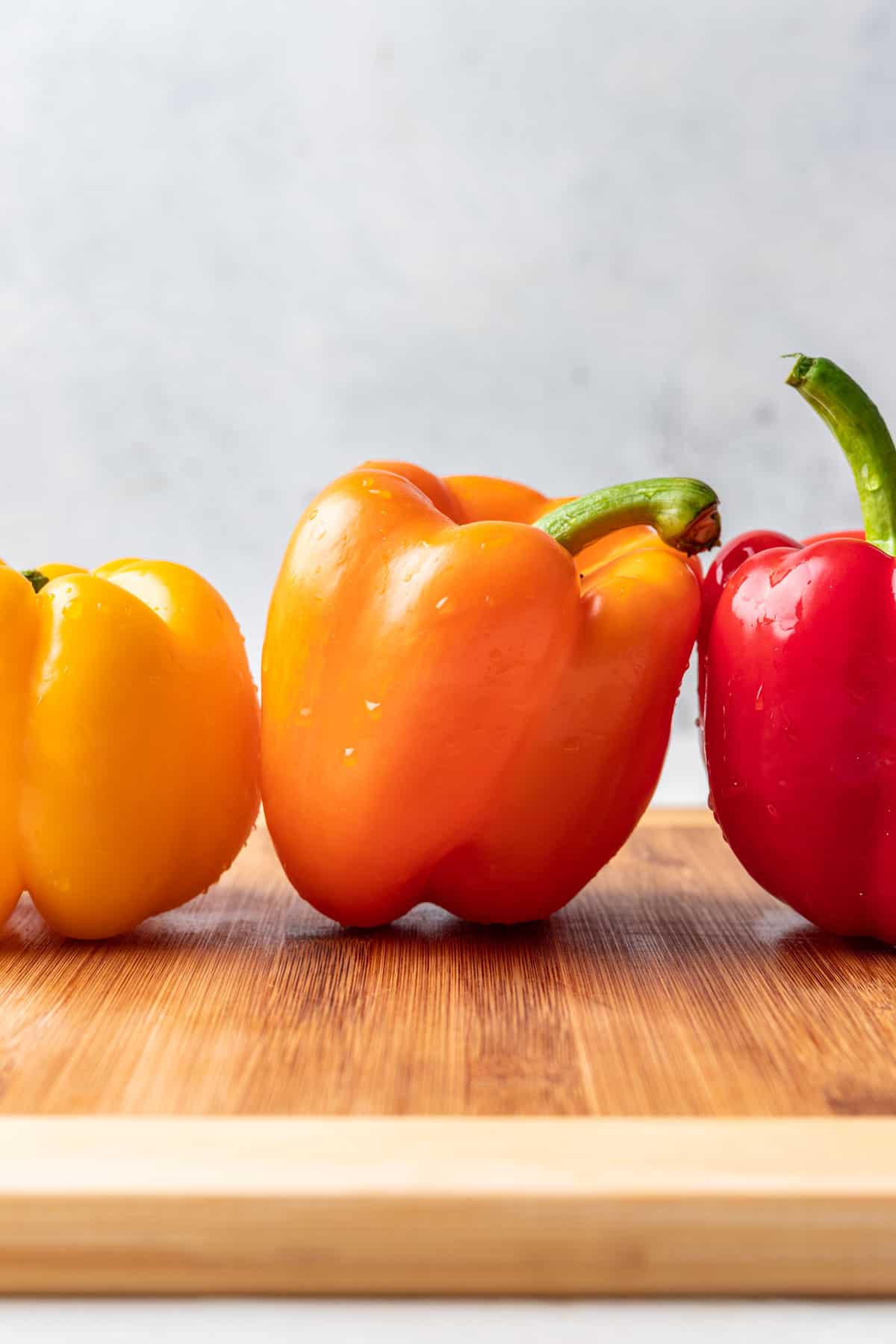 3 bell peppers on a wood cutting board.