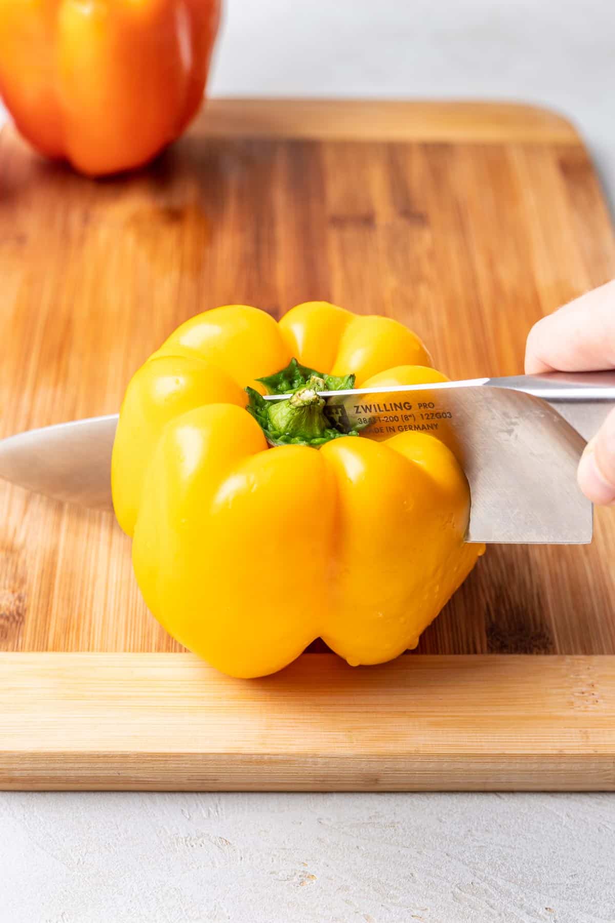 A chef's knife cutting a yellow bell pepper in half.