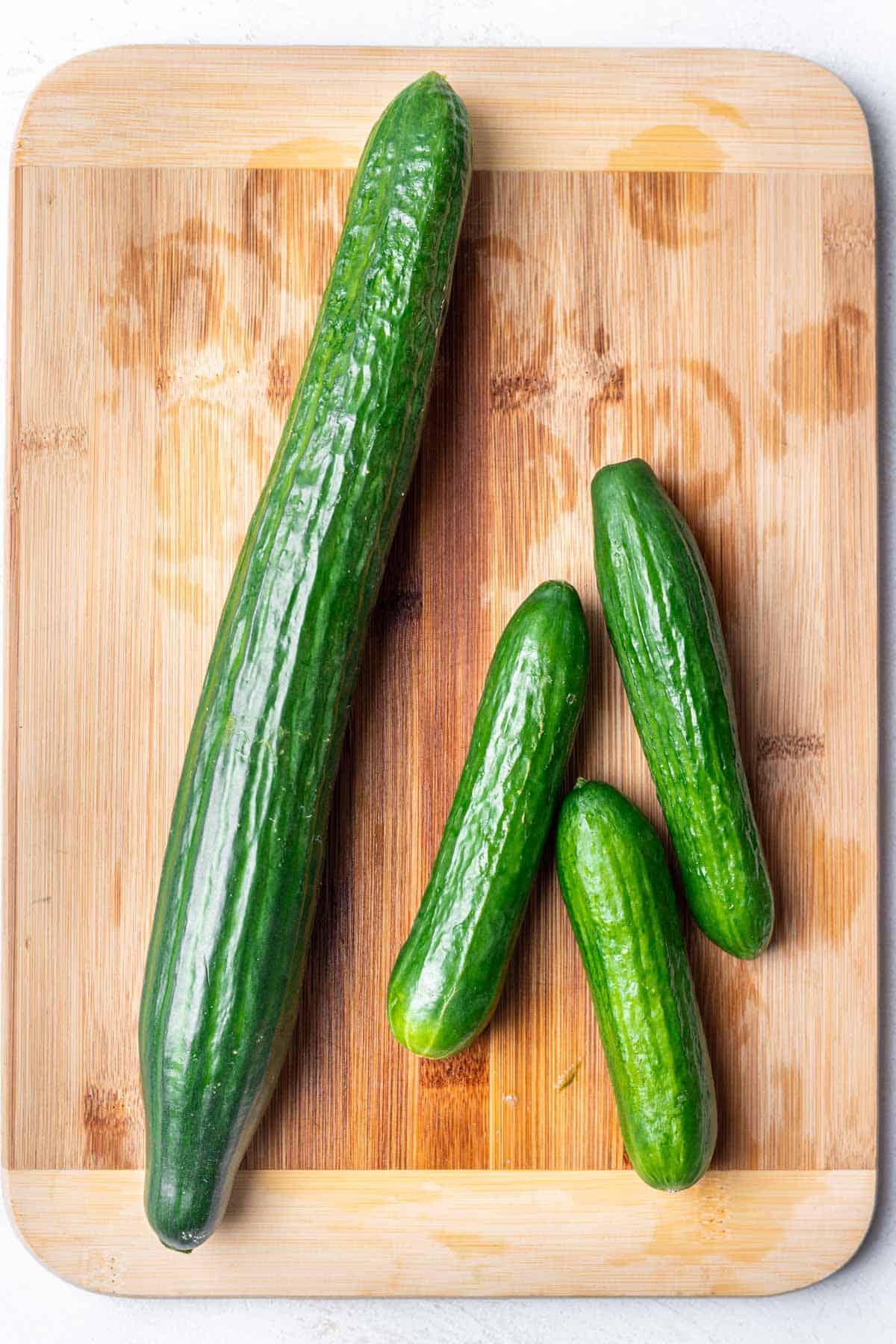 Different sized cucumbers on a cutting board.
