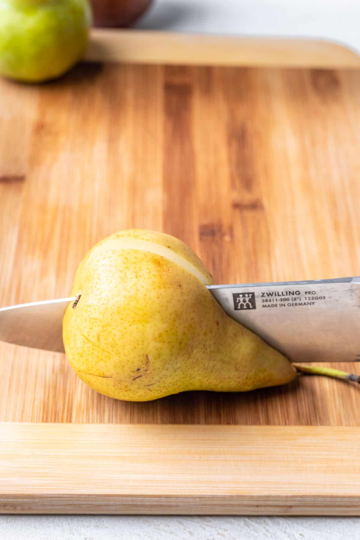 A yellow pear on a wood cutting board, sliced in half with a knife.