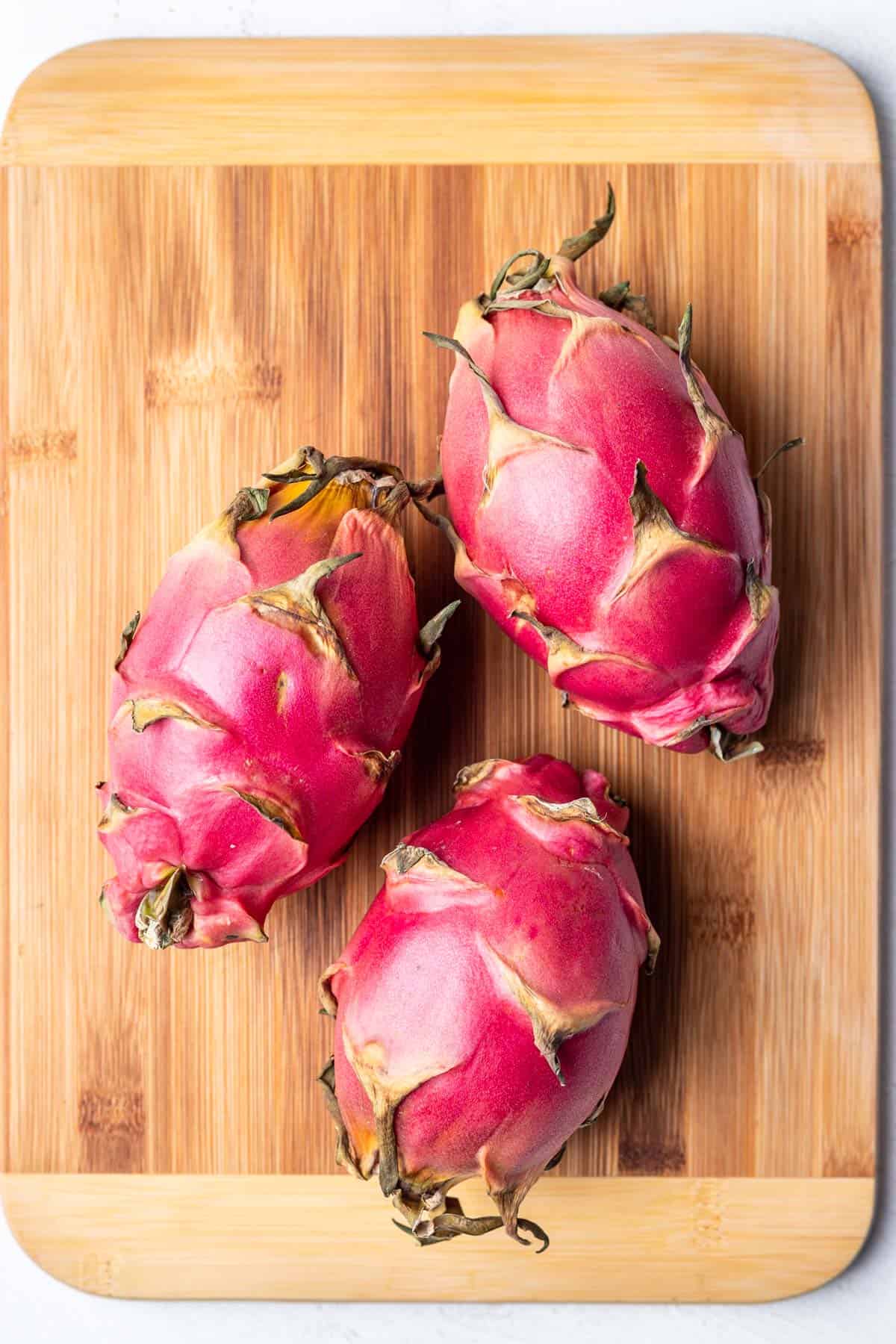 3 whole dragon fruit on a wood cutting board.