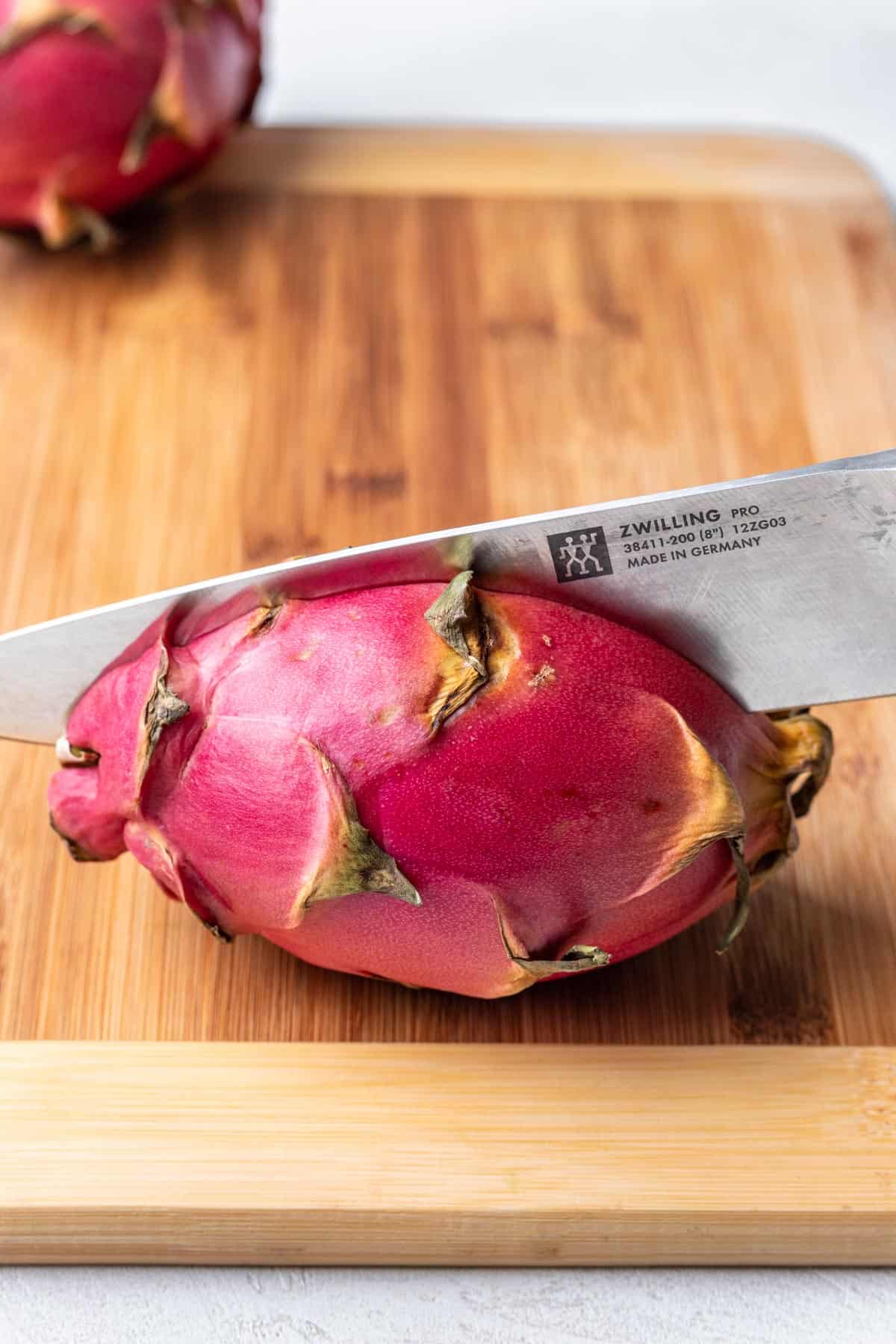 A chef's knife cutting a dragon fruit in half lengthwise.