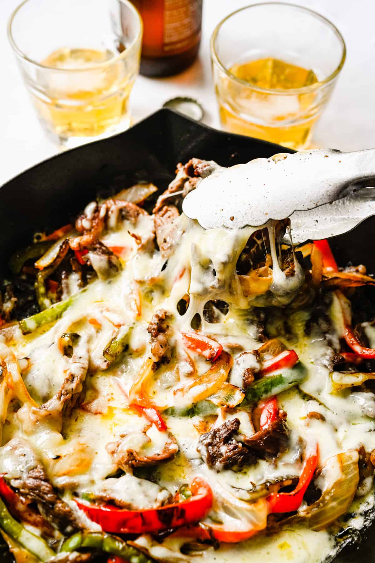 Philly cheesesteak scooped out of a skillet with tongs.