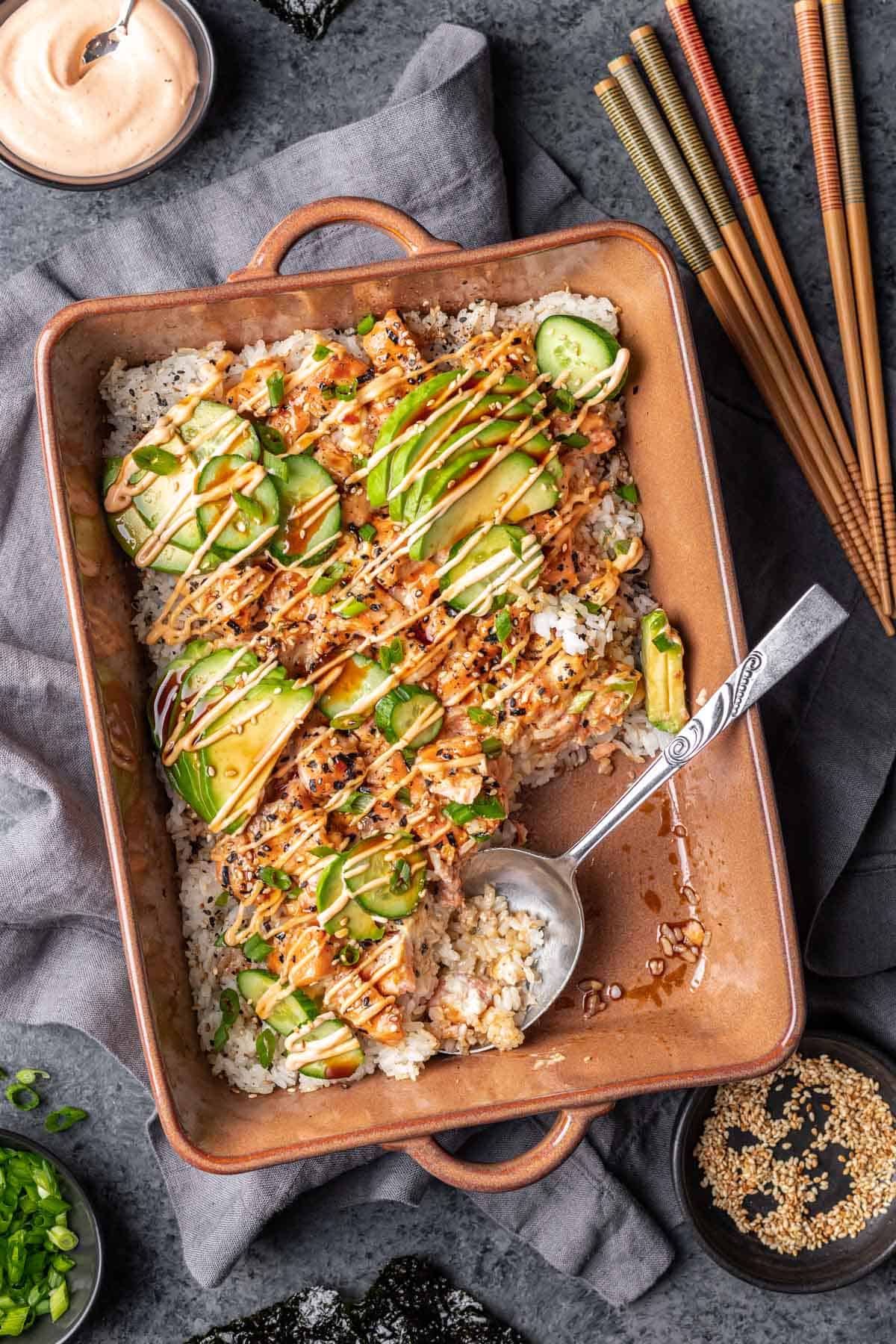 Salmon sushi bake in a baking dish with a serving spoon.