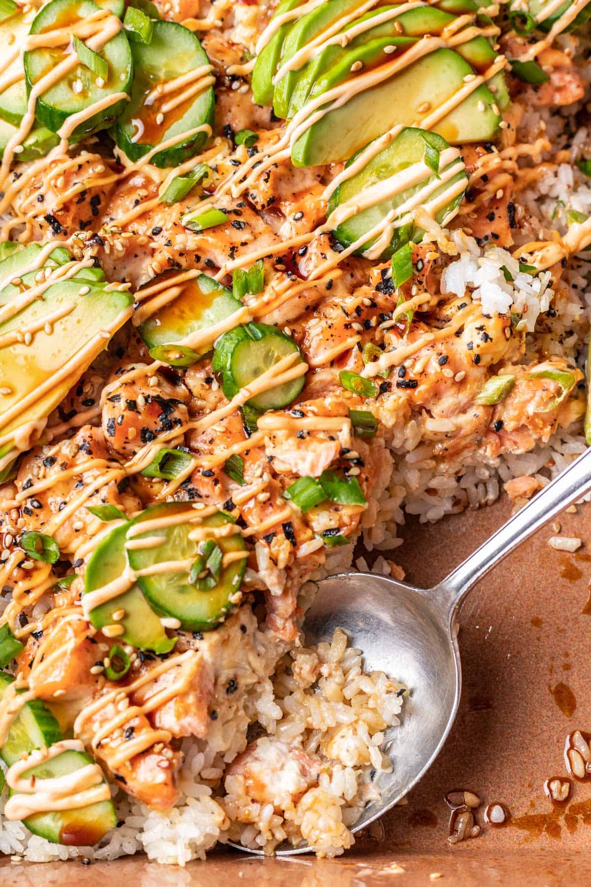 Salmon sushi bake topped with all the sushi fixings and scooped with a serving spoon.
