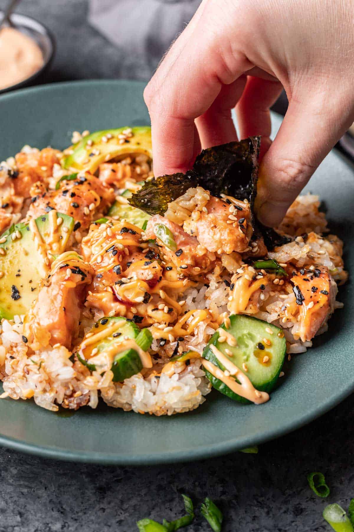 Salmon sushi bake getting scooped up by a hand holding a seaweed snack.