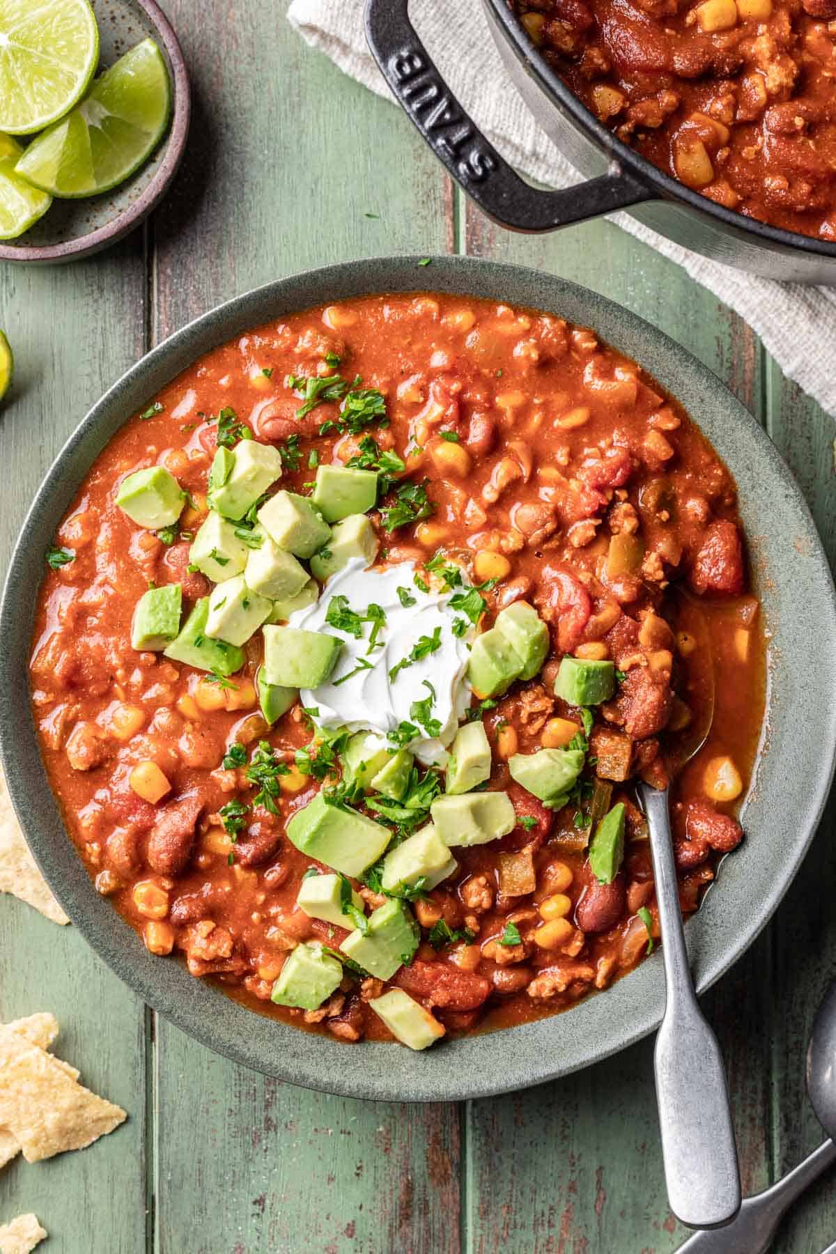 Dutch oven chili in a bowl topped with sour cream, cilantro, and diced avocado.