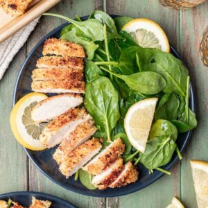 Panko chicken sliced on a plate with a spinach salad.