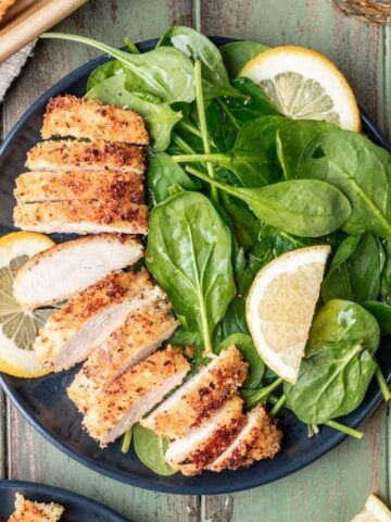 Panko chicken sliced on a plate with a spinach salad.